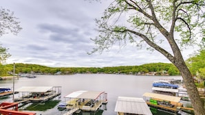 A lakeside dock with several boats, a covered seating area, and a tree in the foreground. - Waterfront Ozarks Home w/ Hot Tub, Bar & Dock (Rocky Mount)