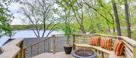 Una terraza de madera con un pozo de fuego y zona de estar con vistas a un lago.