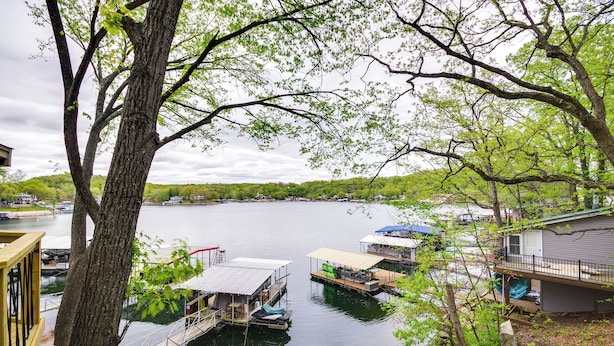 A lakeside property with docked boats, a wooden deck, and a house with a covered porch. - Waterfront Ozarks Home w/ Hot Tub, Bar & Dock (Rocky Mount)