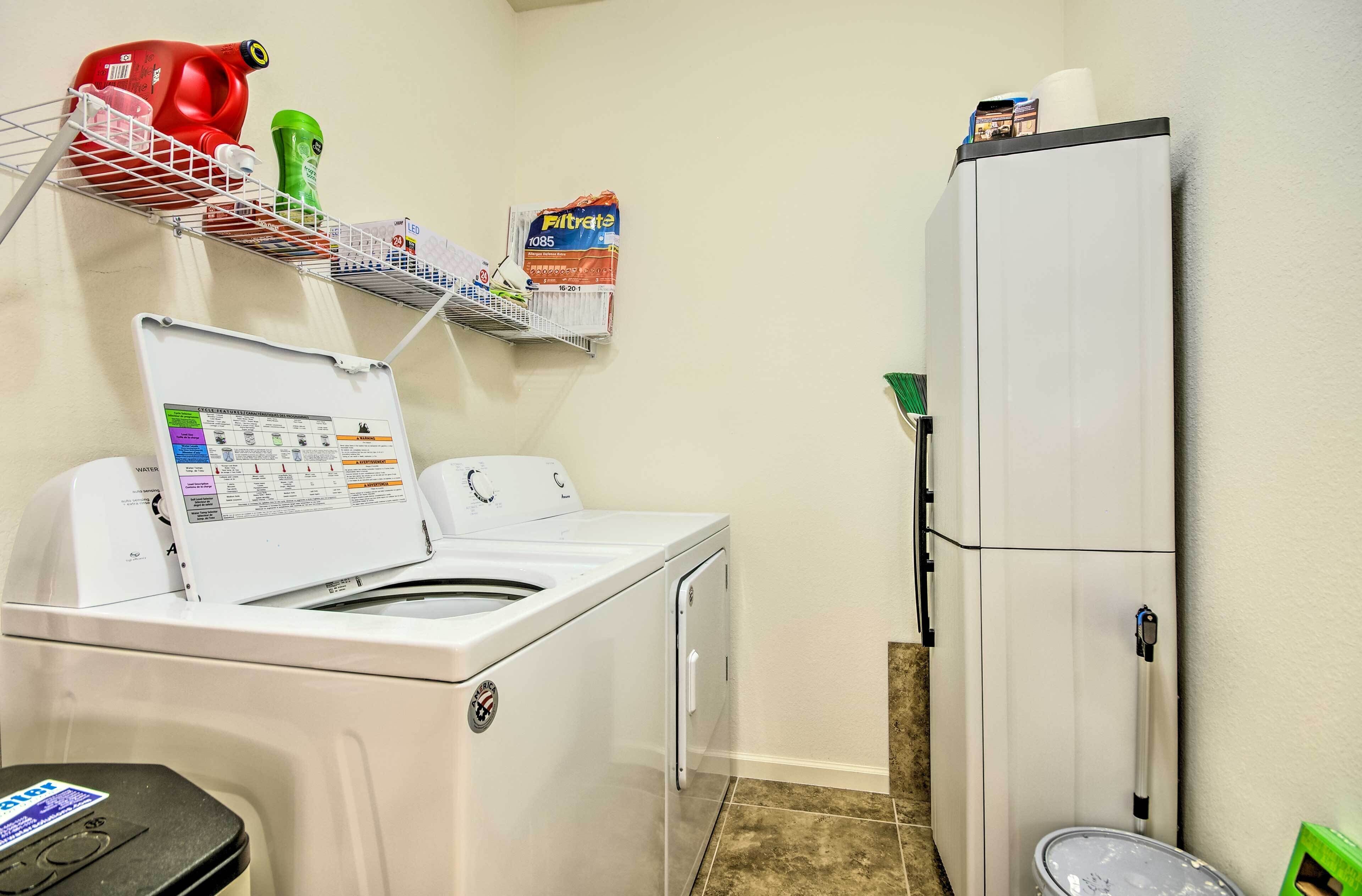 Un área de lavandería con lavadora de carga frontal, un tendedero y un refrigerador.