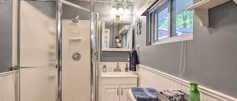Un baño compacto con mampara de vidrio, un lavabo blanco y un espejo encima.