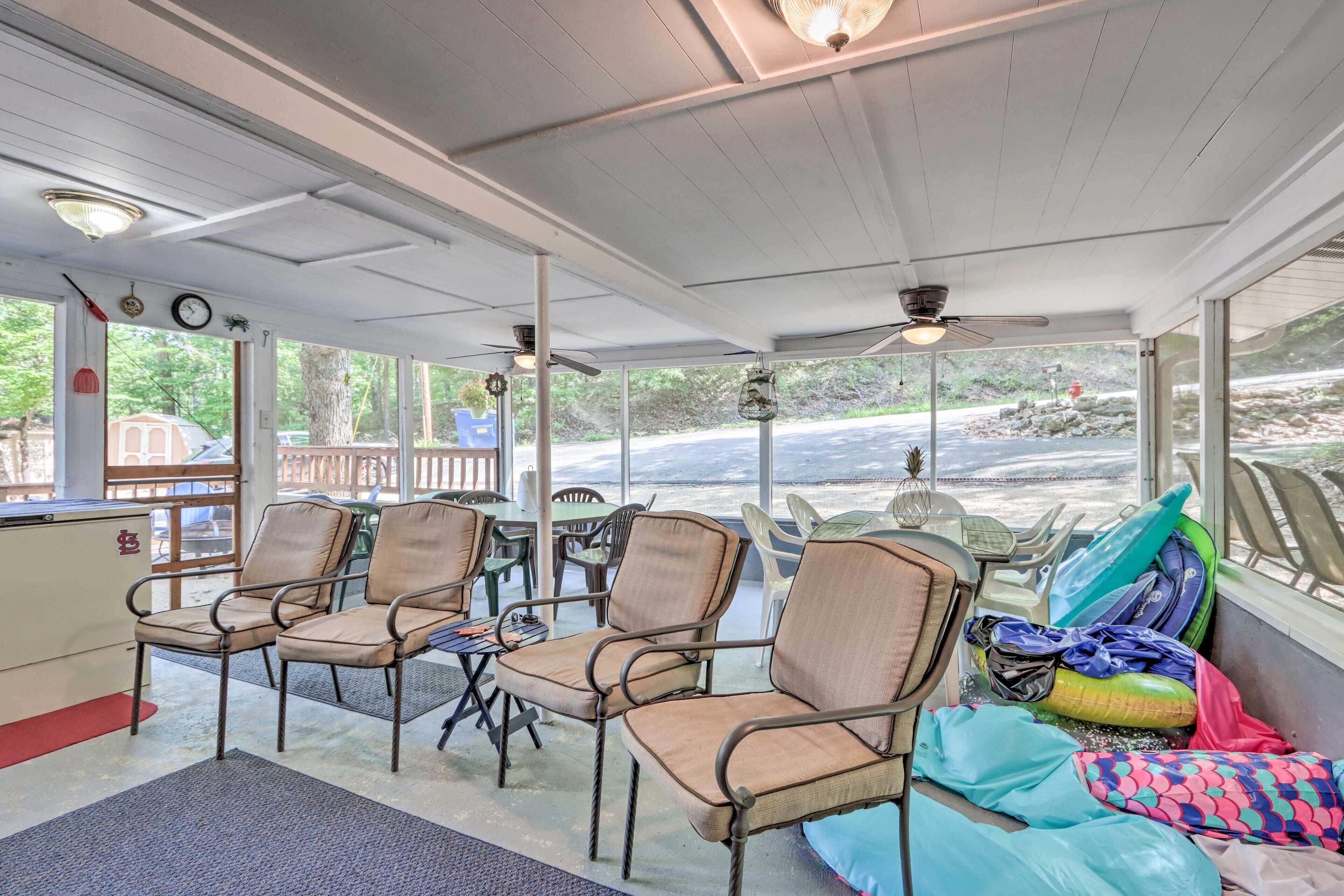 A covered outdoor seating area with wicker chairs, a table, and a ceiling fan.