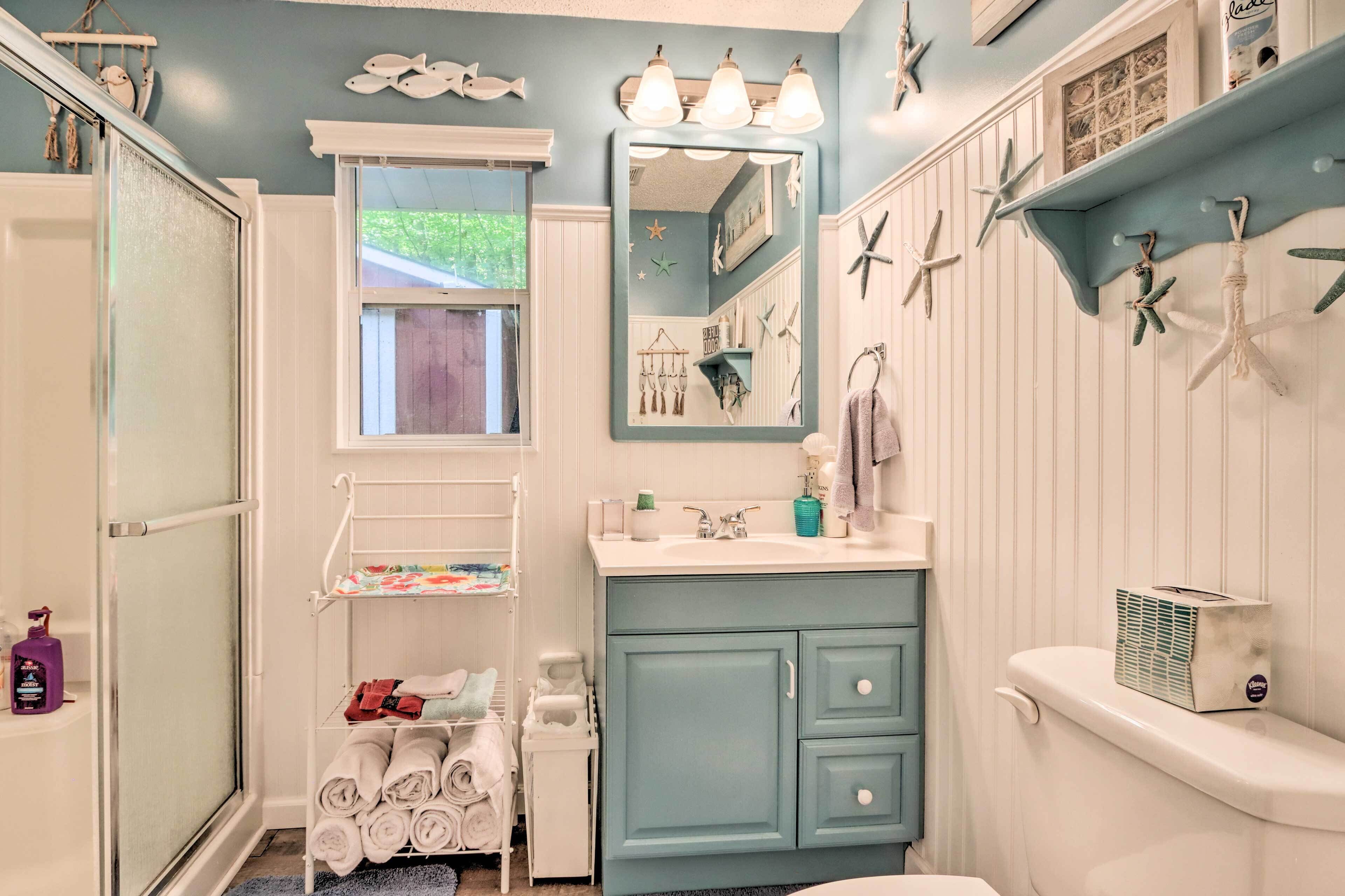 A bathroom with a blue vanity, white cabinets, a white toilet, and a window with a view of greenery.