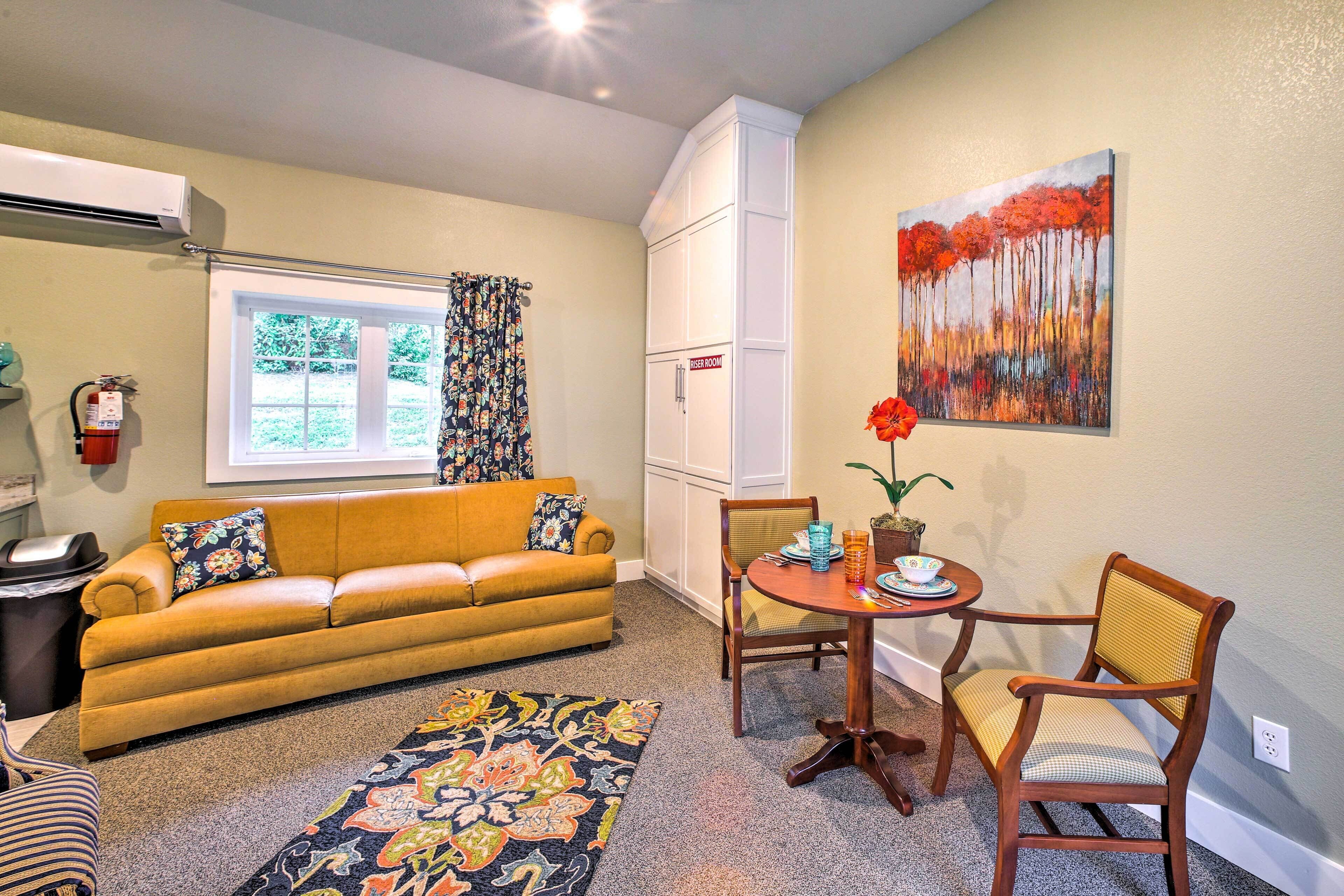 A living room with a sofa, chairs, a small table, a rug, and a painting on the wall.