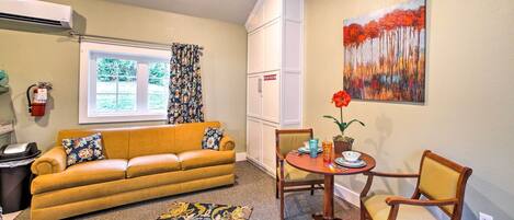 A living room with a sofa, chairs, a small table, a rug, and a painting on the wall.