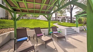 Un área de estar al aire libre con techo, con dos sillones de descanso y una pequeña mesa, rodeada por una estructura de metal verde.