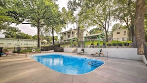 Una piscina con borde curvo, rodeada por un solárium de hormigón. Se observan sillones de descanso y una zona de estar cubierta.