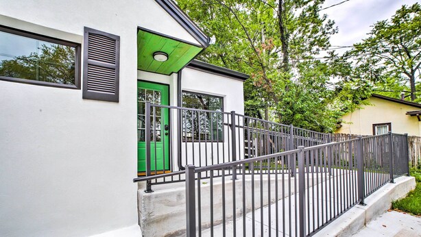 Un edificio moderno con una puerta verde, una cerca metálica y fachada blanca.