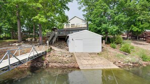A lakeside property with a dock, a covered boat storage area, and a house with a balcony overlooking the water. - Waterfront Lake of the Ozarks Home w/ Views! (Gravois Mills)