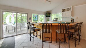 A kitchen with a bar area, sliding glass doors leading to a patio, and a television mounted above the bar. - Waterfront Lake of the Ozarks Home w/ Views! (Gravois Mills)