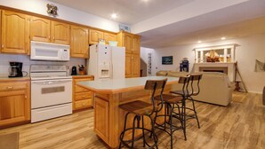 A kitchen with wooden cabinets, a microwave, a refrigerator, and a bar area with stools. - Waterfront Lake of the Ozarks Home w/ Views! (Gravois Mills)