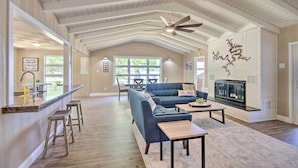 A spacious living room with a high ceiling, a fireplace, and a large window.