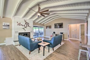 A spacious living room with a high ceiling and exposed beams, a fireplace, and a large window providing natural light. - Dock! Waterfront Family Home on Lake of the Ozarks (Lake Ozark)