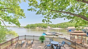 A wooden deck with outdoor furniture overlooking a calm river, surrounded by lush greenery.