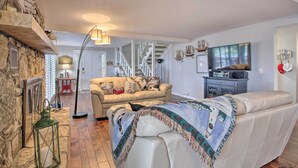 A cozy living room with a stone fireplace, a sofa, a television, and a staircase leading to another level. - Hot Tub, Dock! Waterfront Lake Ozark Home! (Lake Ozark)