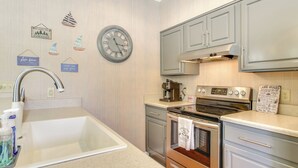 A kitchen with a sink, stove, and cabinets. There are wall decorations and a clock. - Lakefront Mccormick Gem: Deck & Golf Course Views (McCormick)