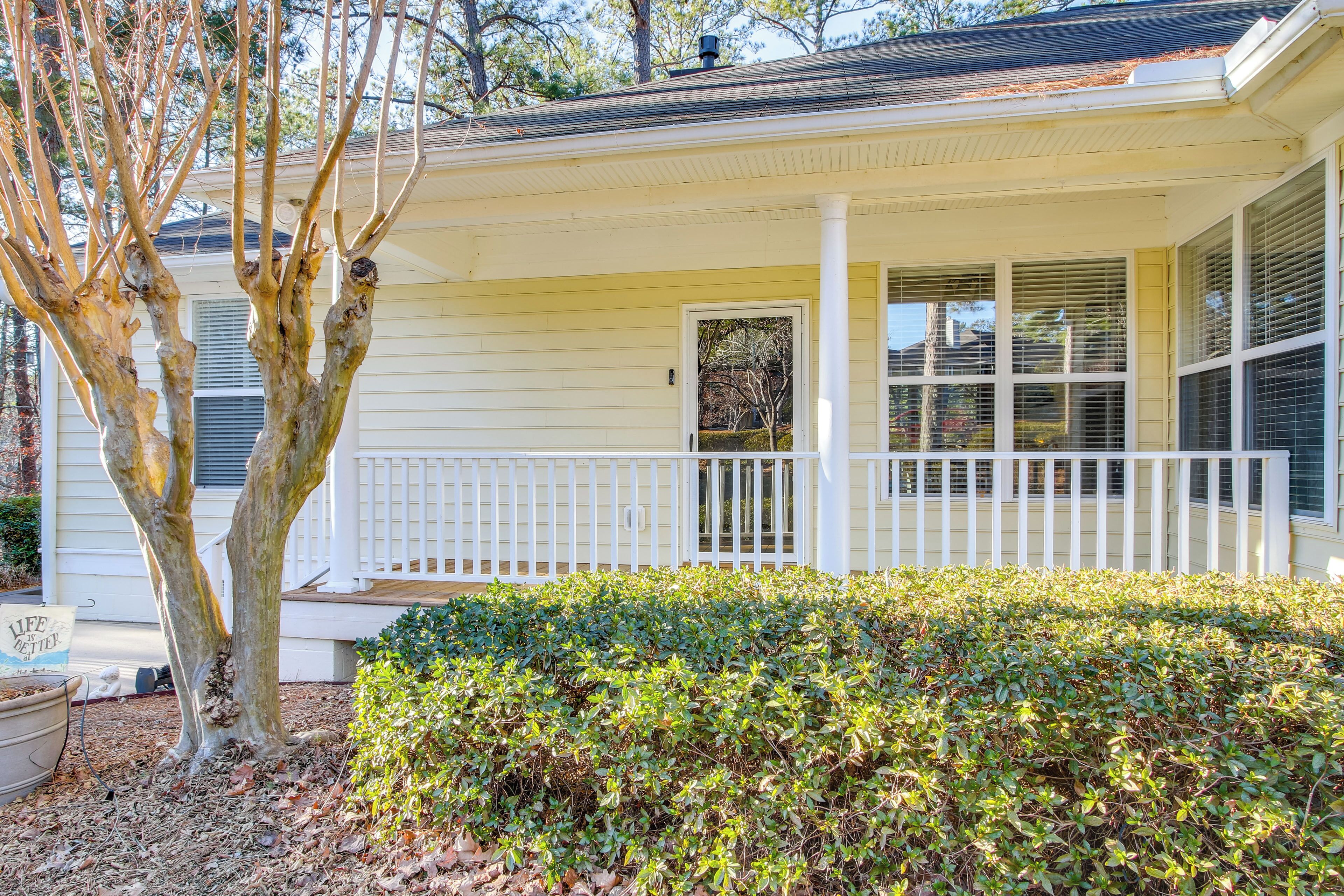 A single-story house with a porch, a small garden, and a tree.