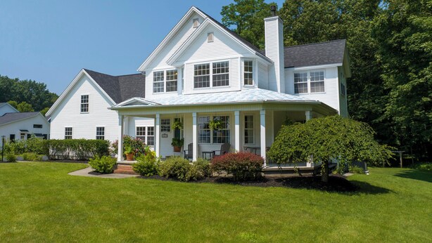 A large, two-story house with a wrap-around porch, surrounded by a well-maintained lawn and mature trees.