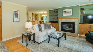 A living room with a sofa, coffee table, and fireplace. There is a kitchen in the background.