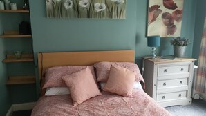 Un dormitorio con cama, mesita de noche, cómoda y dos cuadros en la pared.