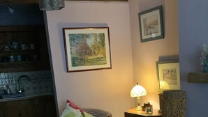 Una sala de estar acogedora con un sofá de cuero negro, una mesa de centro de madera y una mesita auxiliar con una lámpara. Hay un cuadro en la pared y una cesta de mimbre en el suelo.