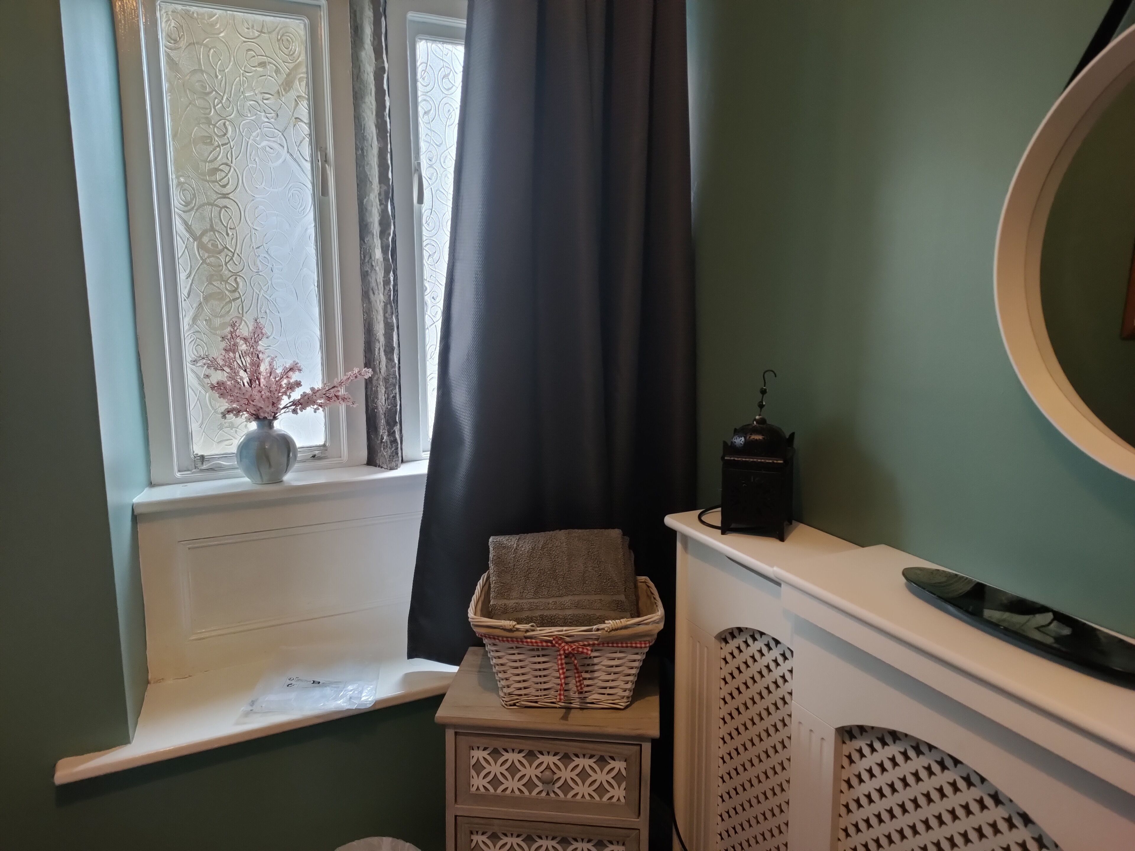 A bathroom with a window, a vase with flowers, a basket, and a towel on a shelf.