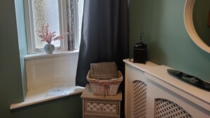Un baño con ventana, un florero con flores, una cesta y una toalla en un estante.