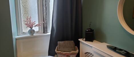 A bathroom with a window, a vase with flowers, a basket, and a towel on a shelf.