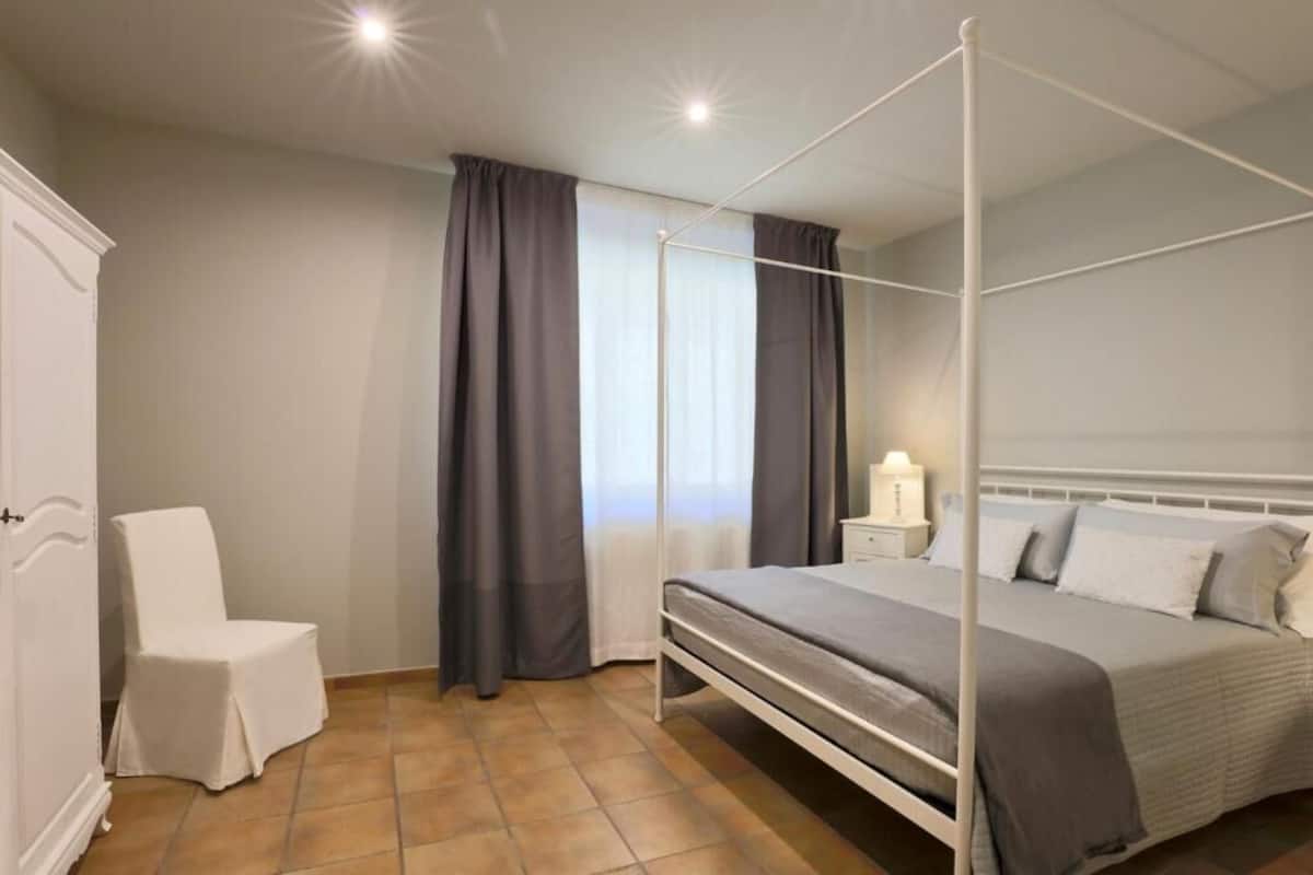 A bedroom with a four-poster bed, a bedside table with a lamp, a chair, and a wardrobe.