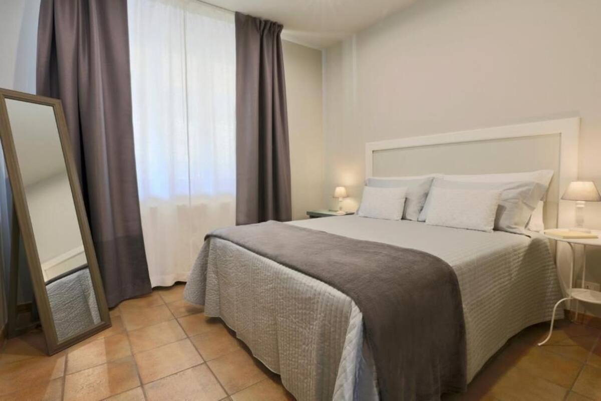A hotel room with a large bed, a bedside table with a lamp, a mirror, and a window with curtains.