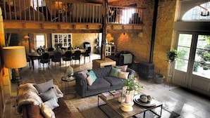 A rustic interior with a high ceiling, exposed wooden beams, a dining area, and a cozy seating area with a fireplace. - Maison des Quatre Saisons (Les Esseintes)