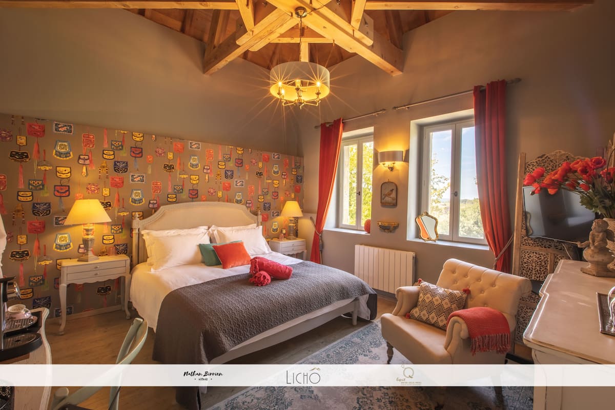 Une chambre à coucher comprenant un lit, des tables de chevet, une commode, une fenêtre avec des rideaux et un lustre.