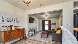 A living room with a wooden floor, a grey sofa, a white armchair, a wooden cabinet, and a ceiling fan. - Cozy Home w/ Spacious yard<br>Hunters welcomed (Haskell)
