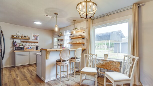 A kitchen with wooden flooring, white cabinetry, a central island with bar stools, and a large window with curtains. - Cozy Home w/ Spacious yard<br>Hunters welcomed (Haskell)