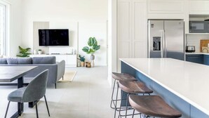 Moderni keittiö, jossa on valkoiset kaapit, suuri keittiösaareke ja baarituolit.