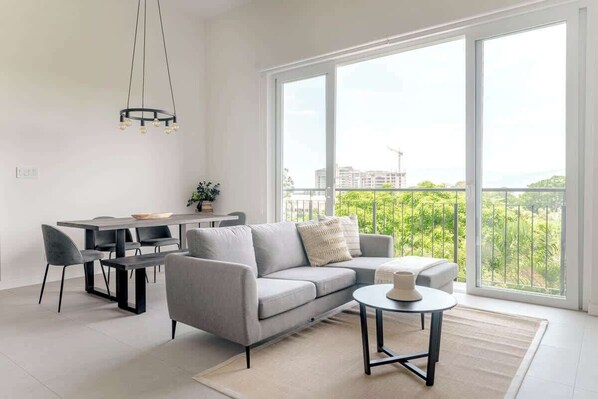 Uma sala de estar moderna com um sofá cinzento, uma mesa de centro redonda e uma área de jantar com mesa e cadeiras.