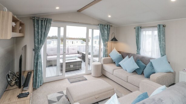 A modern living room with a sofa, ottoman, and a television on a wooden stand. - Rowan Court 2 (Scarborough)