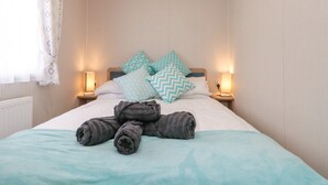 A neatly made bed with rolled towels, two bedside lamps, and patterned pillows. - Rowan Court 2 (Scarborough)