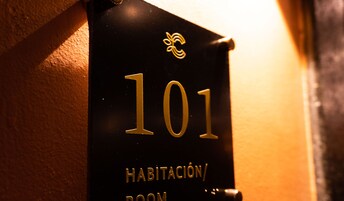 Primer plano de un cartel negro con el número 101 y la inscripción “HABITACIÓN ROOM” en letras doradas.