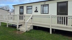 A mobile home with a front porch, a staircase, and a window with a curtain. - 2 Bedroom Caravan Hunstanton Pets go Free (Hunstanton)