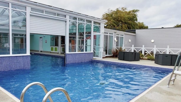 A swimming pool with a clear blue water, surrounded by a building with large windows and a covered patio area. - 2 Bedroom Caravan Hunstanton Pets go Free (Hunstanton)