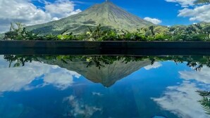 A mountain with a clear reflection in a body of water, surrounded by greenery. - Best Villa (La Fortuna)