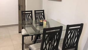 Un coin repas avec une table en verre et des chaises noires, un tableau au mur et une porte dotée d’une poignée.