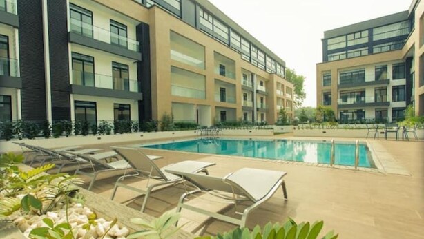 A modern building with a swimming pool, lounge chairs, and potted plants. - Cozy Studio Apartment in heart of Cantonment (Accra)
