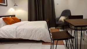 A hotel room with a bed, a desk, a chair, and a curtain. - Cozy Studio Apartment in heart of Cantonment (Accra)