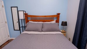 A bedroom with a wooden headboard, a bed with a grey quilt, a nightstand with a lamp, and a door. - Little Cottage on the Field (Buckingham)