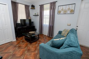 A living room with a sofa, a glass coffee table, a TV on a stand, and patterned flooring. - Little Cottage on the Field (Buckingham)