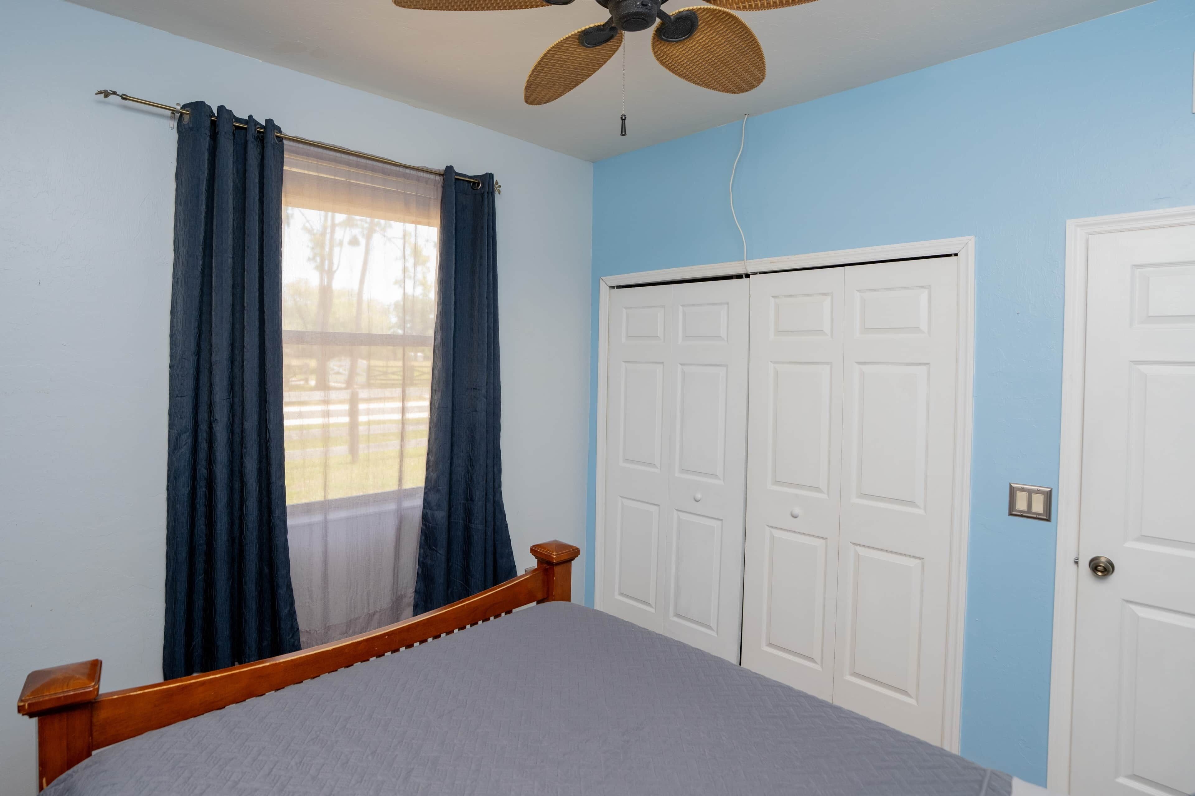 Une chambre à coucher avec un lit, un ventilateur de plafond, une fenêtre avec des rideaux et un ensemble de portes blanches.