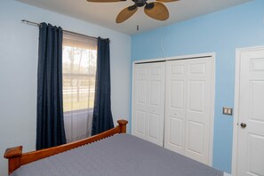 A bedroom with a bed, a ceiling fan, a window with curtains, and a set of white doors. - Little Cottage on the Field (Buckingham)
