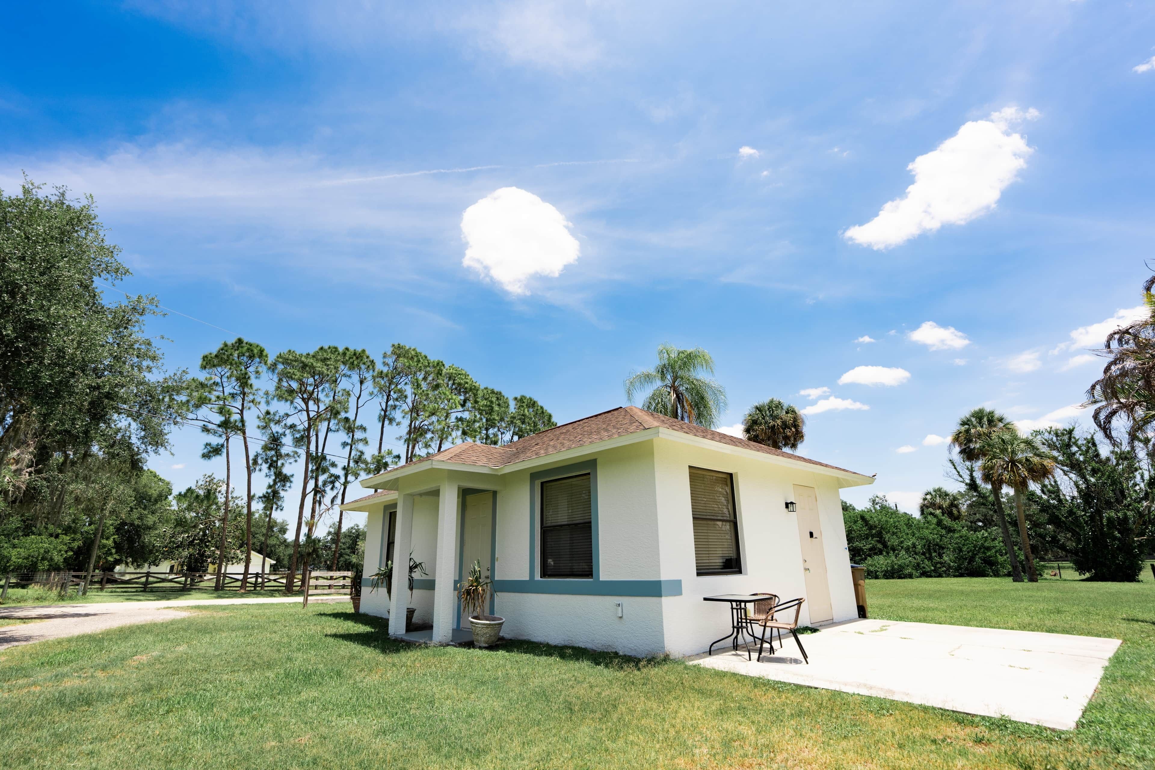 A small, single-story building with a flat roof, a front porch, and a patio area with a table and chairs.